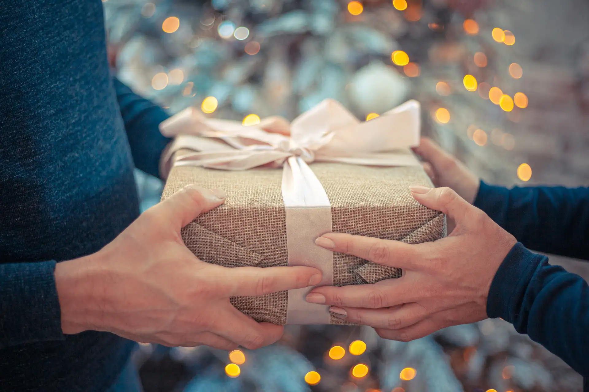 In the picture, a close-up of the hands of two people exchanging a gift.