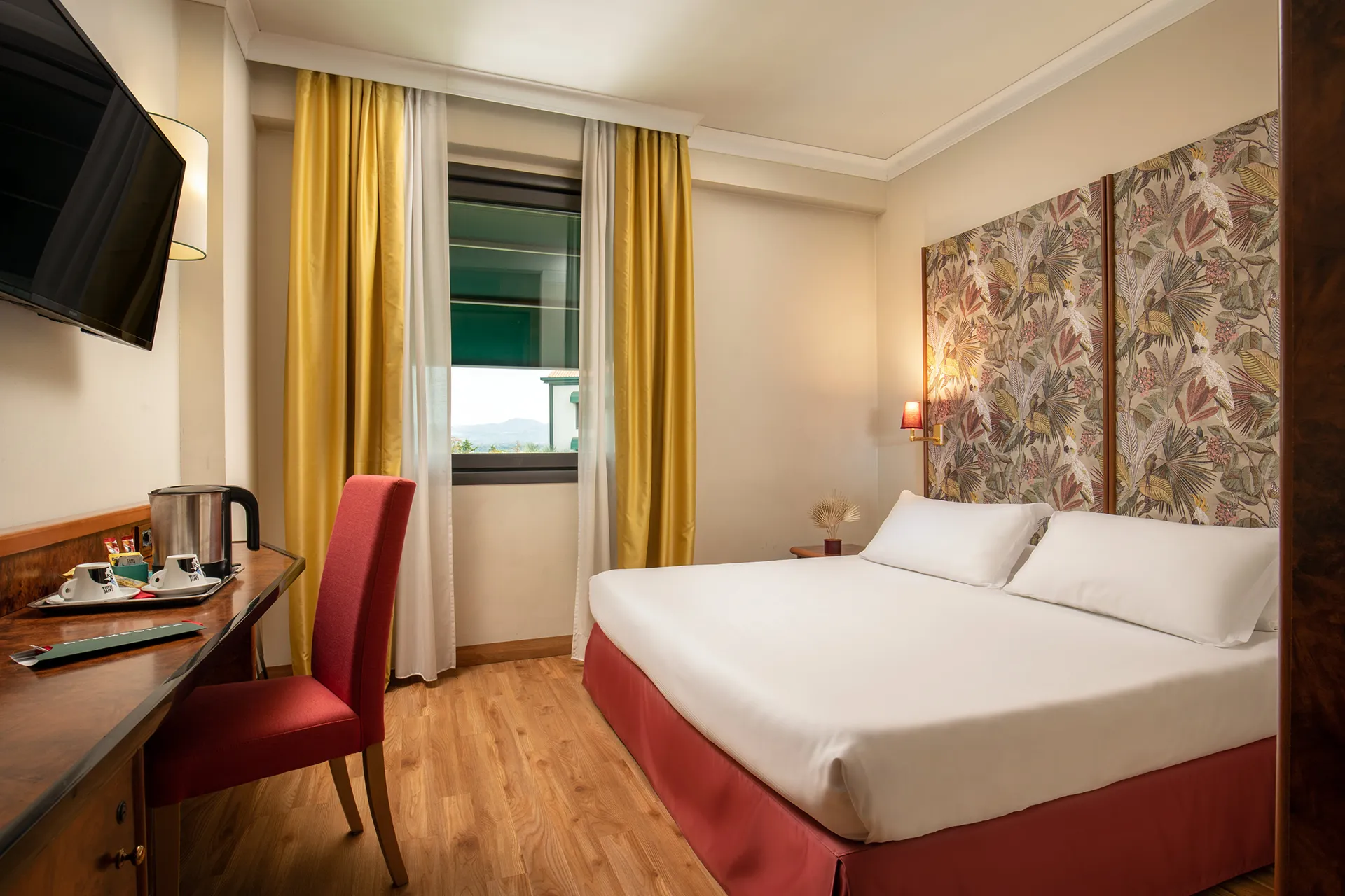 In the picture, the Comfort Room of the Park Hotel Roma Nord: we can see the double bed and, on the other side of the room, a table with a kettle and two cups. A TV is hanging on the wall.